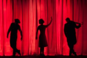 Actors stand silhouetted against a red curtain on a stage. See a show at Dr. Phillips Center for the Performing Arts on Valentine's Day.